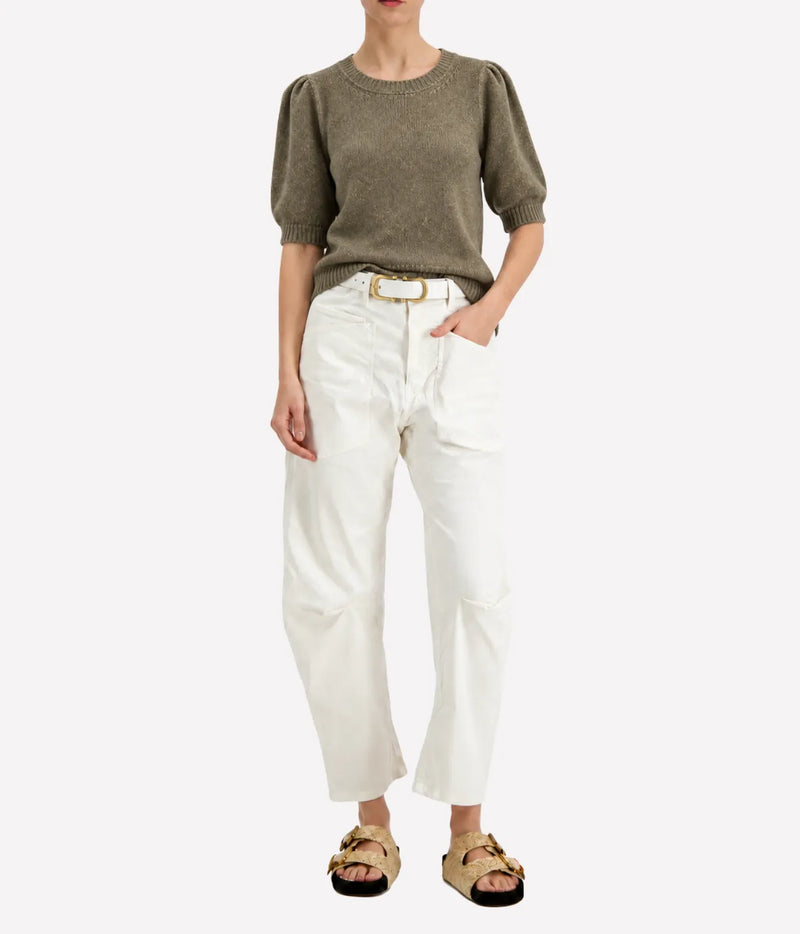 Model wearing the Avant Toi Cashmere Short Sleeve in Mushroom tucked into cream barrel-leg trousers with one hand in her pocket and dark sandals