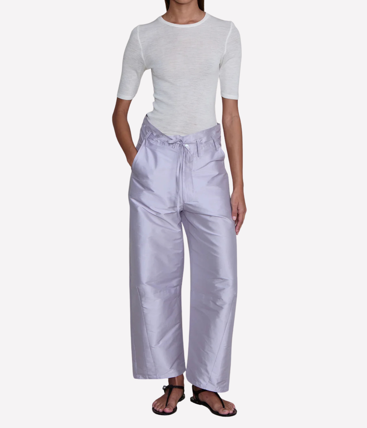 Front view of a model wearing the Chan Luu Techno Taffeta Barrel Pant in Lilac with a fitted white short-sleeve top and black thong sandals, showing the high waist, front tie and wide curved barrel leg