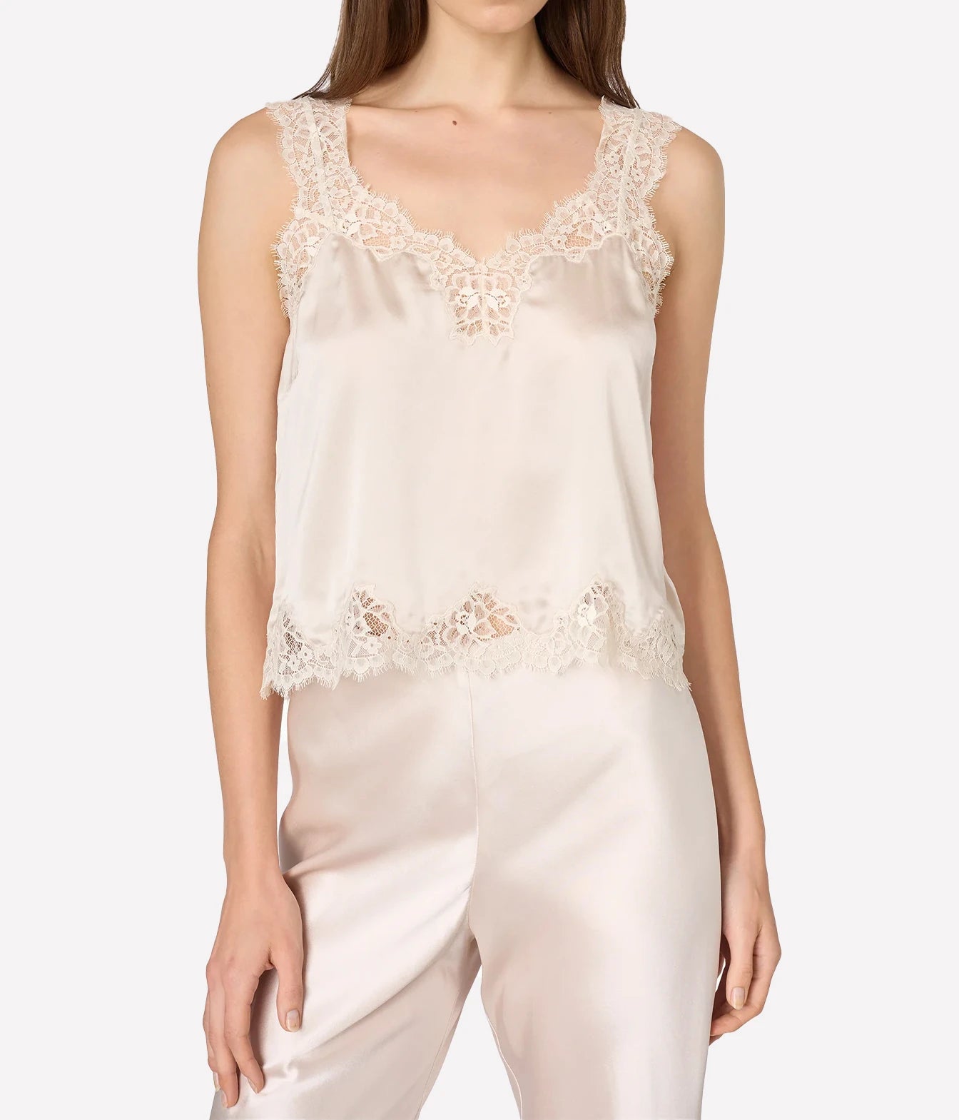 A woman wearing a light beige satin camisole top with intricate lace trim at the scoop neckline and hem
