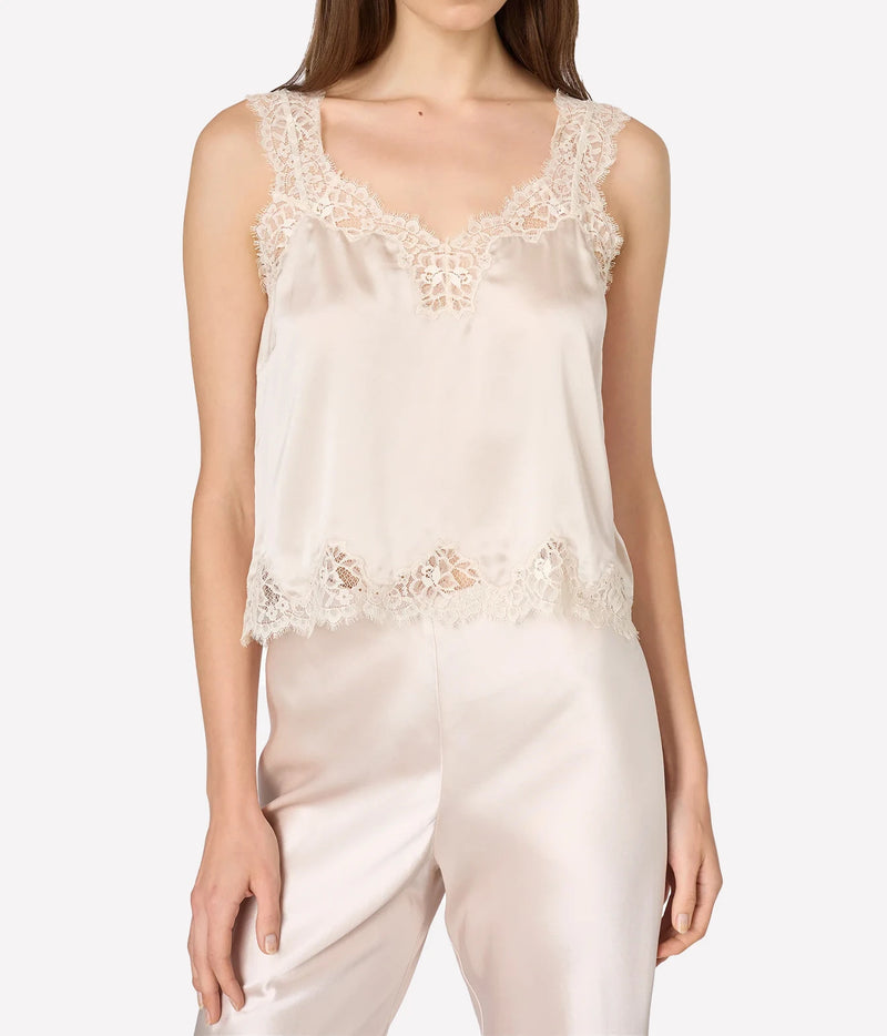 A woman wearing a light beige satin camisole top with intricate lace trim at the scoop neckline and hem