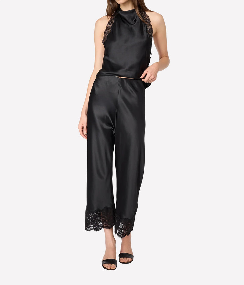 A model wearing a black satin two-piece set consisting of a sleeveless mock-neck top with lace shoulder detailing 