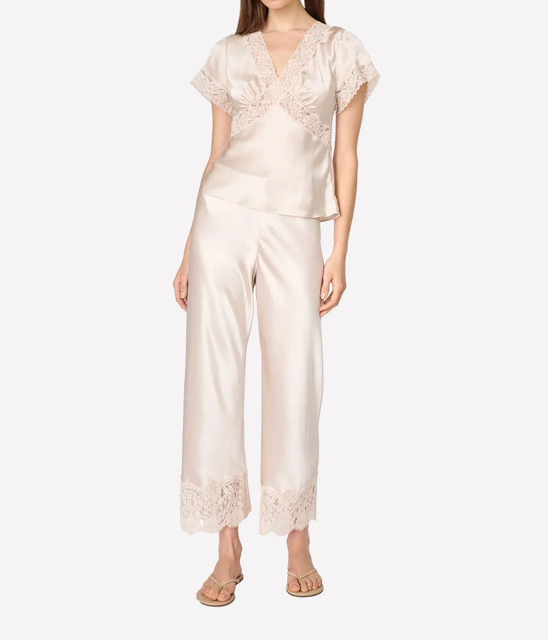 A woman modeling a two-piece satin set in a warm cream color, featuring a short-sleeve top with lace trim