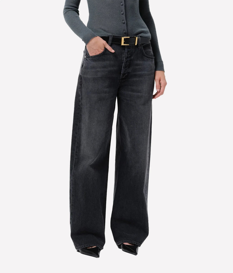 A model wearing wide-leg dark gray denim jeans with a black belt featuring a gold buckle, styled with a gray long-sleeve top against a light gray background.