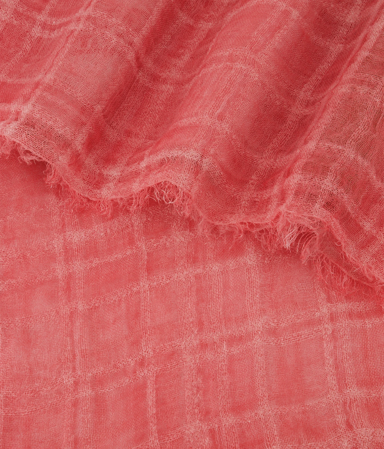 A close-up of a coral pink lightweight fabric with a subtle plaid pattern and frayed edges, draped to show its texture and weave.