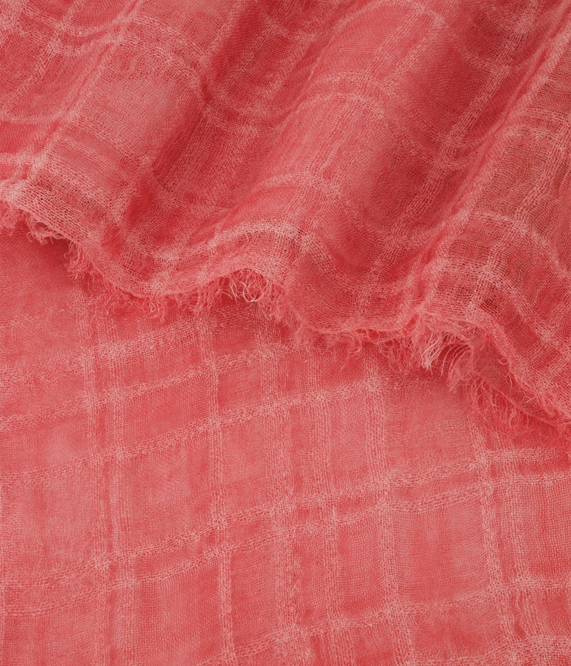 A close-up of a coral pink lightweight fabric with a subtle plaid pattern and frayed edges, draped to show its texture and weave.