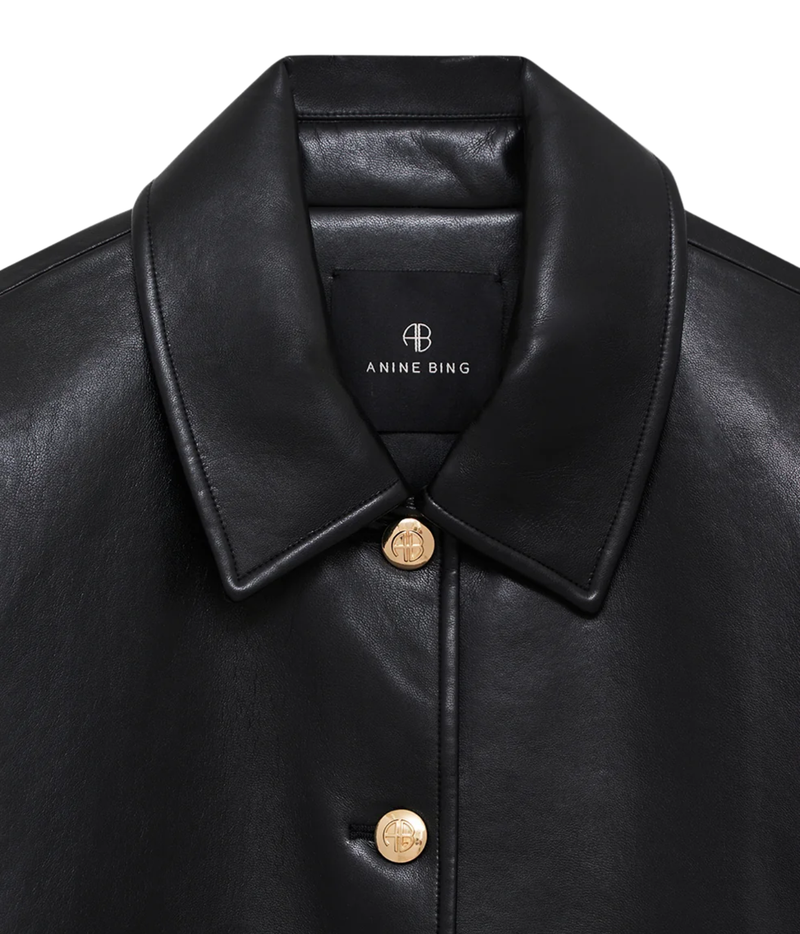 Close-up of a black leather Anine Bing jacket with a structured collar and gold-tone buttons, shown against a plain white background.