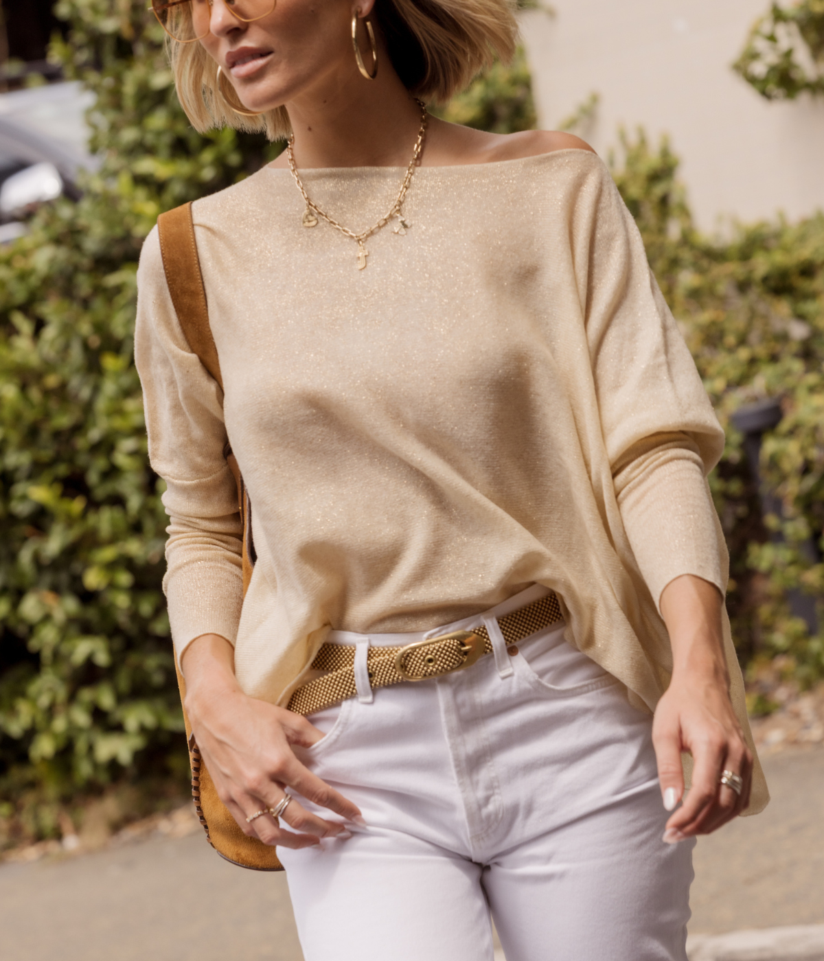 Woman wearing a beige sweater and white pants with a blurred background