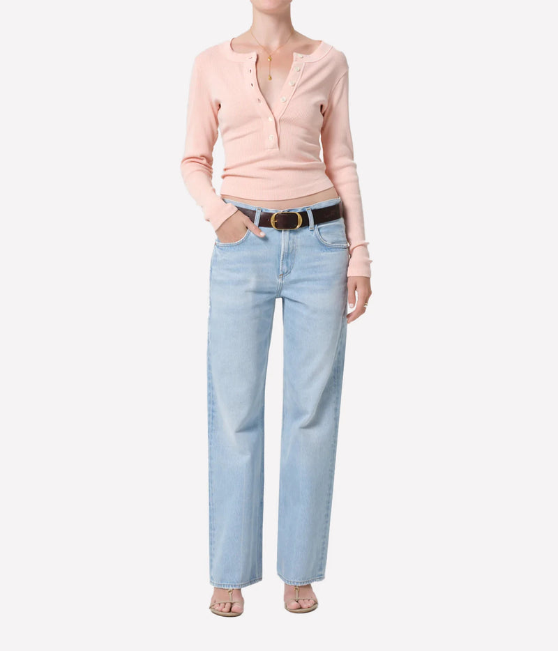 A model wearing a light pink long-sleeve henley top, light blue straight-leg jeans, and a black belt, shown against a plain white background.