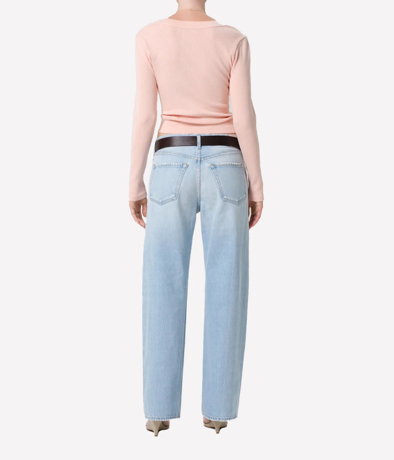A model shown from the back wearing a light pink long-sleeve top, light-wash blue jeans with a black belt, and beige pointed-toe heels against a plain white background.