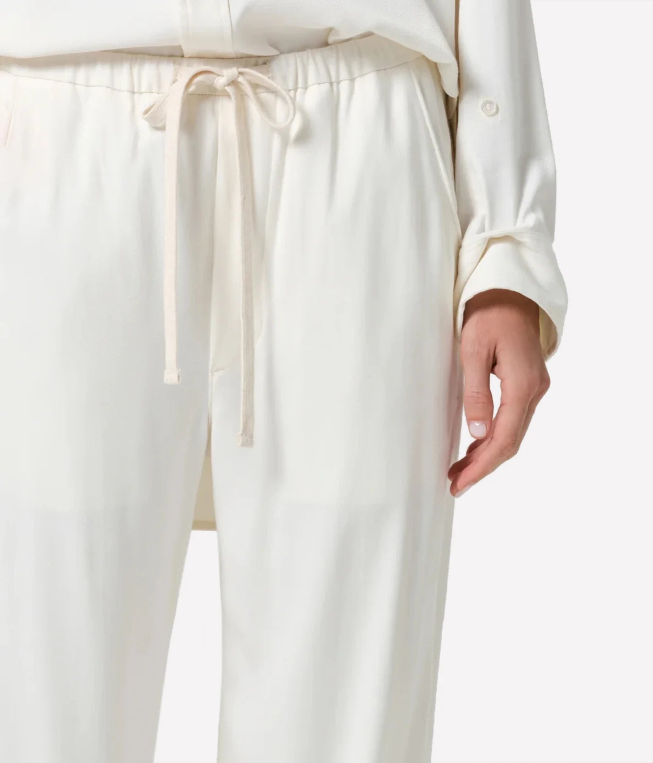 Close-up of a person wearing cream-colored wide-leg trousers with an elastic waistband and matching drawstring tie, paired with a matching cream top against a plain light background.
