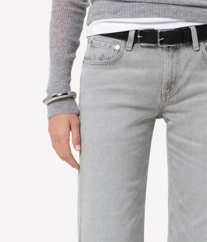 Close-up of a person wearing light gray denim jeans with a black belt, a gray ribbed sweater, and a white undershirt, against a plain light gray background.