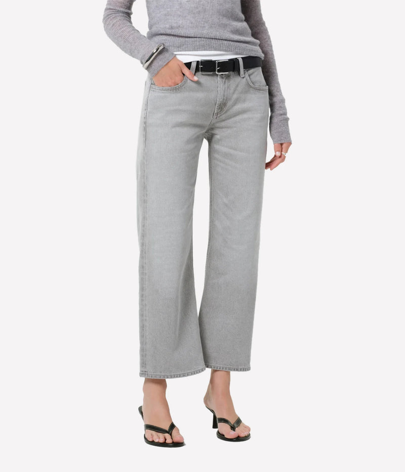 A model wearing light gray cropped wide-leg jeans with a black belt, paired with a gray long-sleeve top and black sandals, against a plain light gray background.