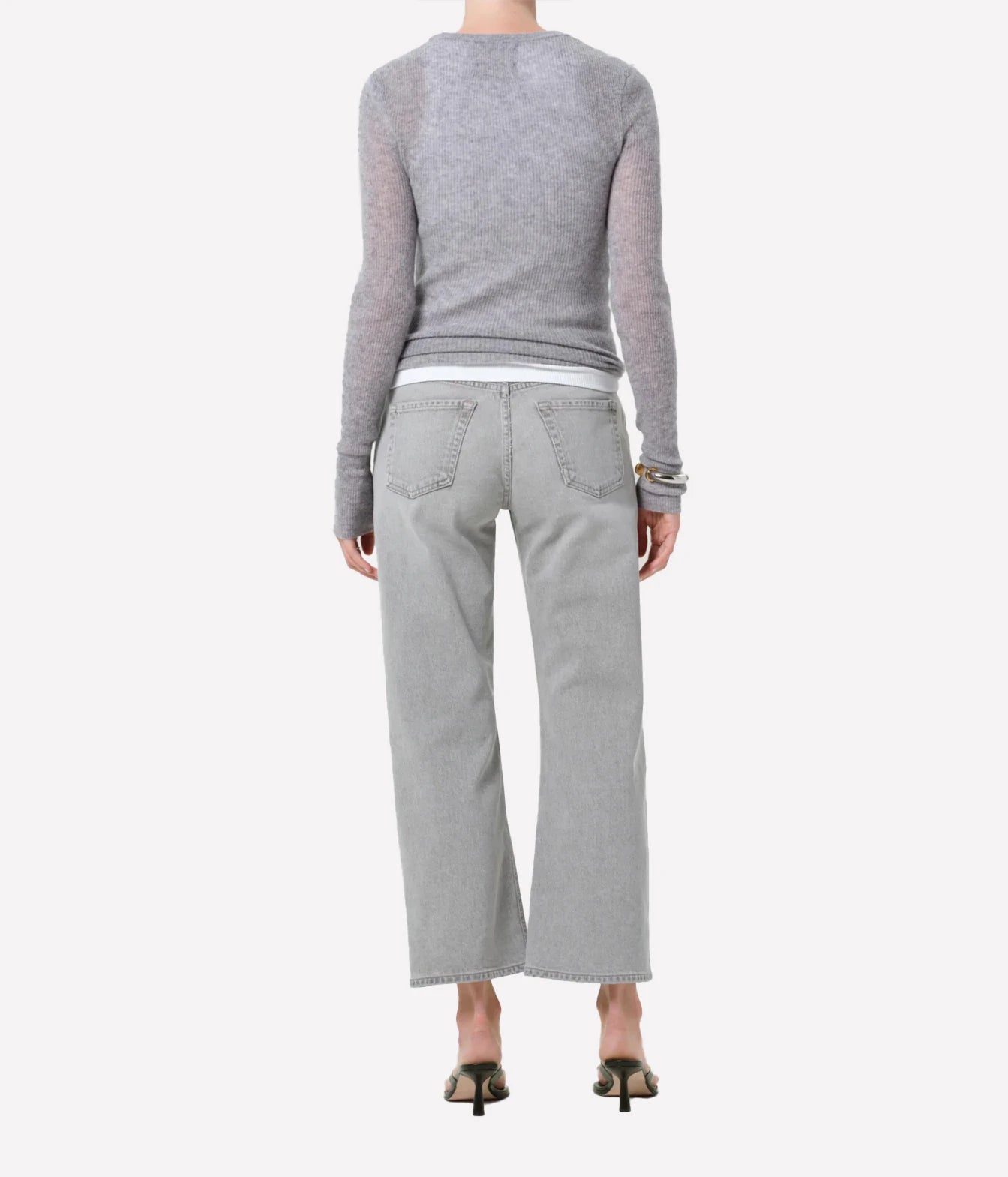 Rear view of a model wearing light gray wide-leg jeans, a heather gray long-sleeve knit top, and black heeled sandals against a plain light gray background.