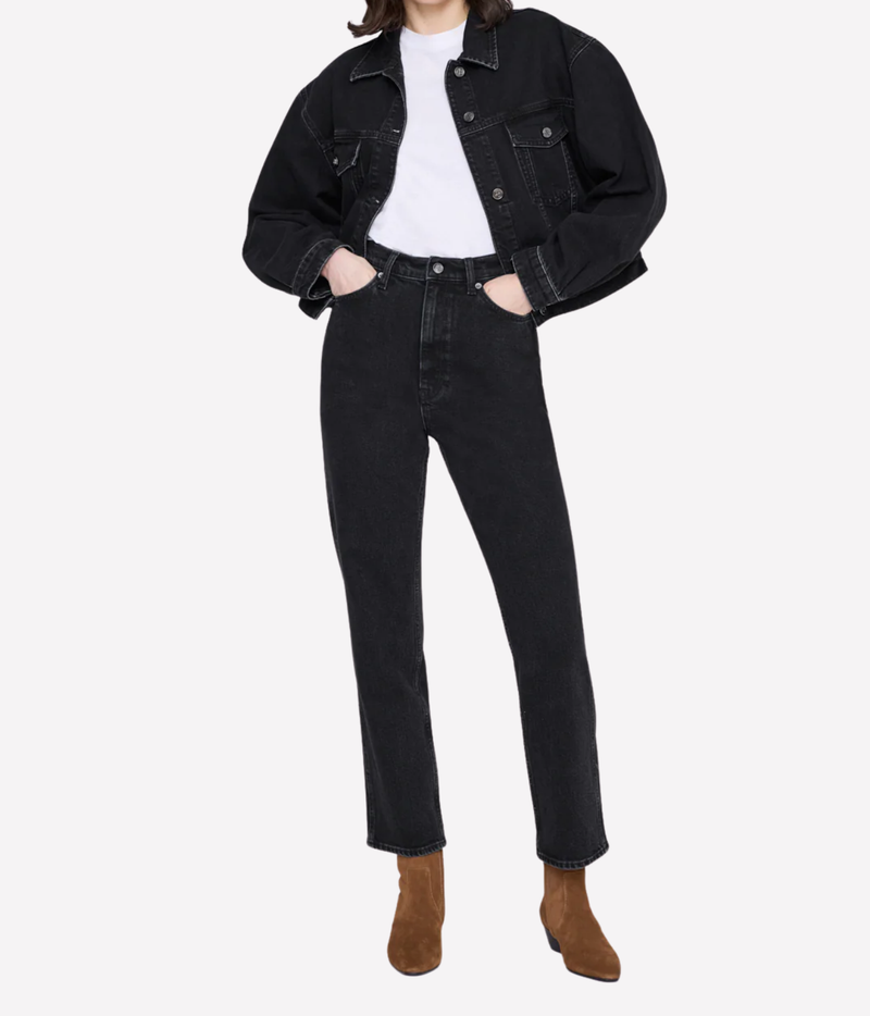 A model wearing a black cropped denim jacket over a white t-shirt, paired with black straight-leg jeans and brown suede ankle boots, shot against a light gray studio background.