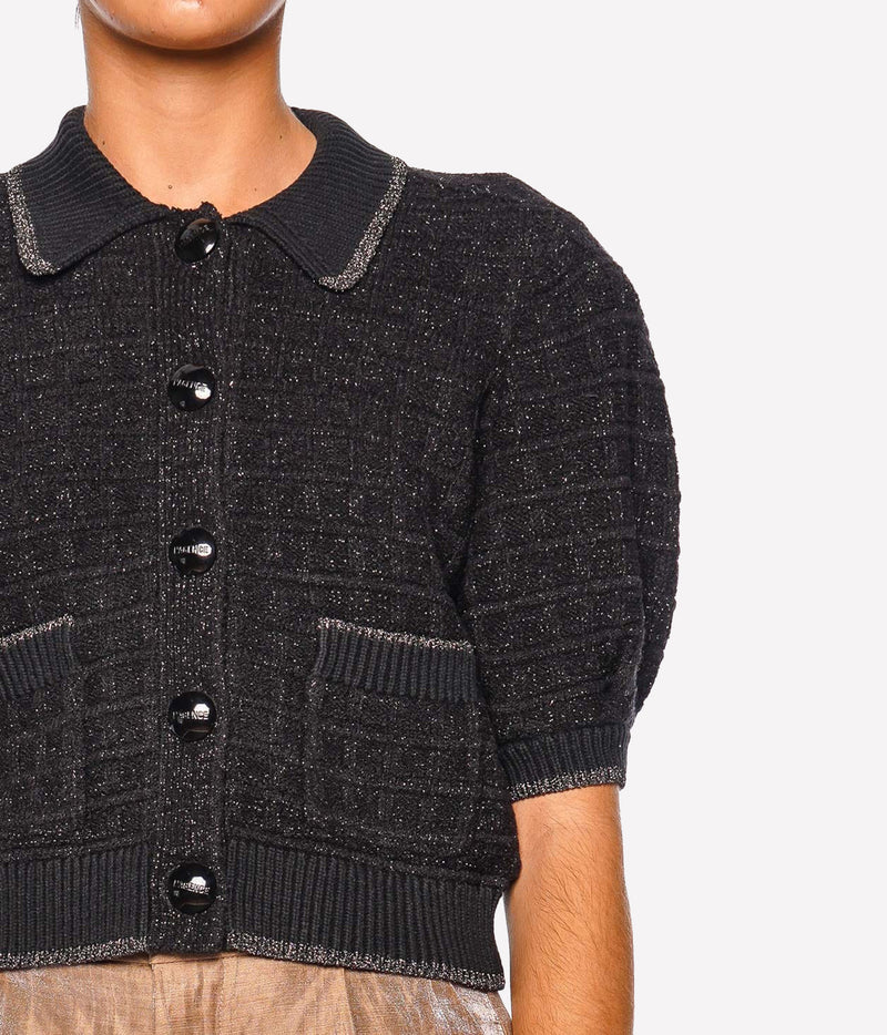 A close-up of a model wearing a black textured knit cardigan with a pointed collar, black buttons, and short puff sleeves.