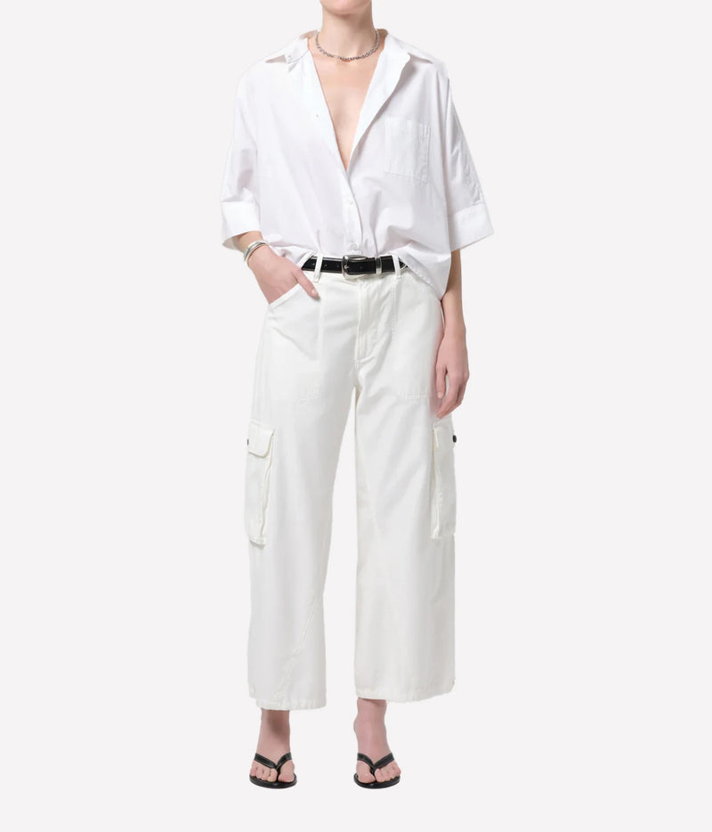 A model wearing a white short-sleeve button-up shirt and white wide-leg cargo pants with a black belt, styled with black flip-flop sandals against a light gray background.