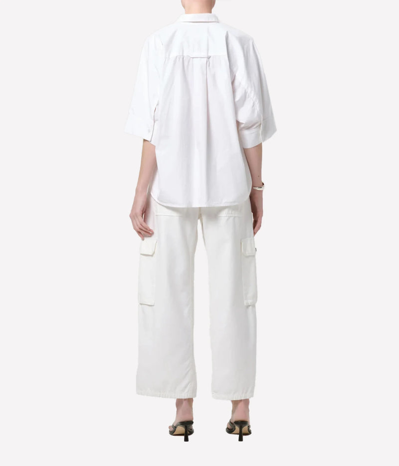 A model shown from the back wearing a white short-sleeve button-up shirt and matching white cargo pants, paired with black heeled sandals, against a light gray studio background.