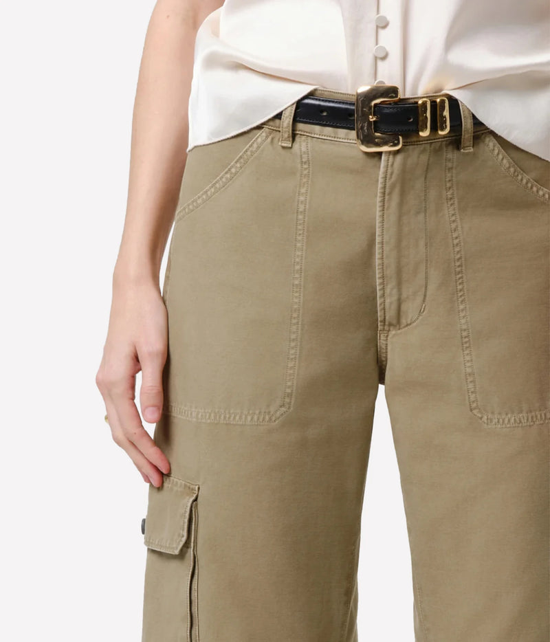A close-up of a person wearing khaki cargo pants with a black belt featuring a gold buckle, paired with a cream-colored blouse against a plain white background.