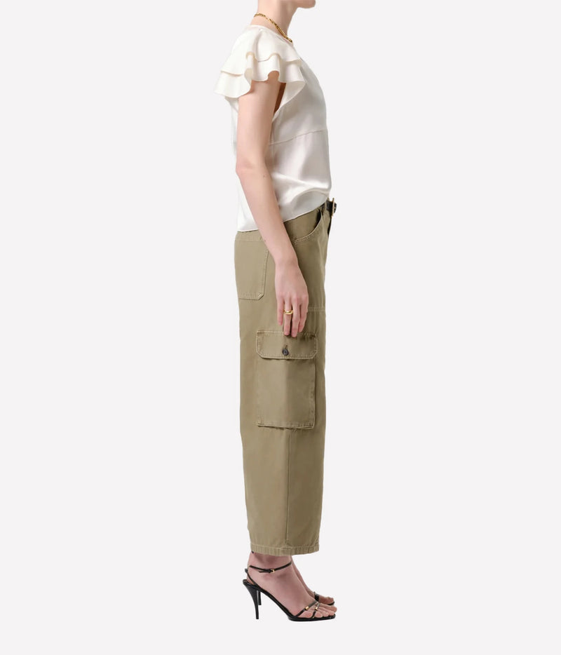 A side-profile view of a model wearing a cream ruffled short-sleeve blouse and olive green cargo pants with black high-heeled sandals, set against a plain light gray background.