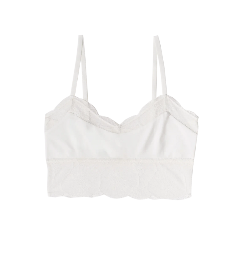 A white camisole-style bralette with thin straps, scalloped lace trim along the neckline and bottom hem, and a structured cup shape, Anemone Cropped Cami In Ivory