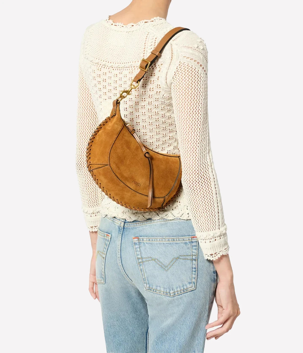 A model from behind wearing a cream-coloured crochet knit sweater and light blue jeans, carrying Oskan moon shoulder bag in braided suede calfskin leather, a crescent-shaped shoulder bag