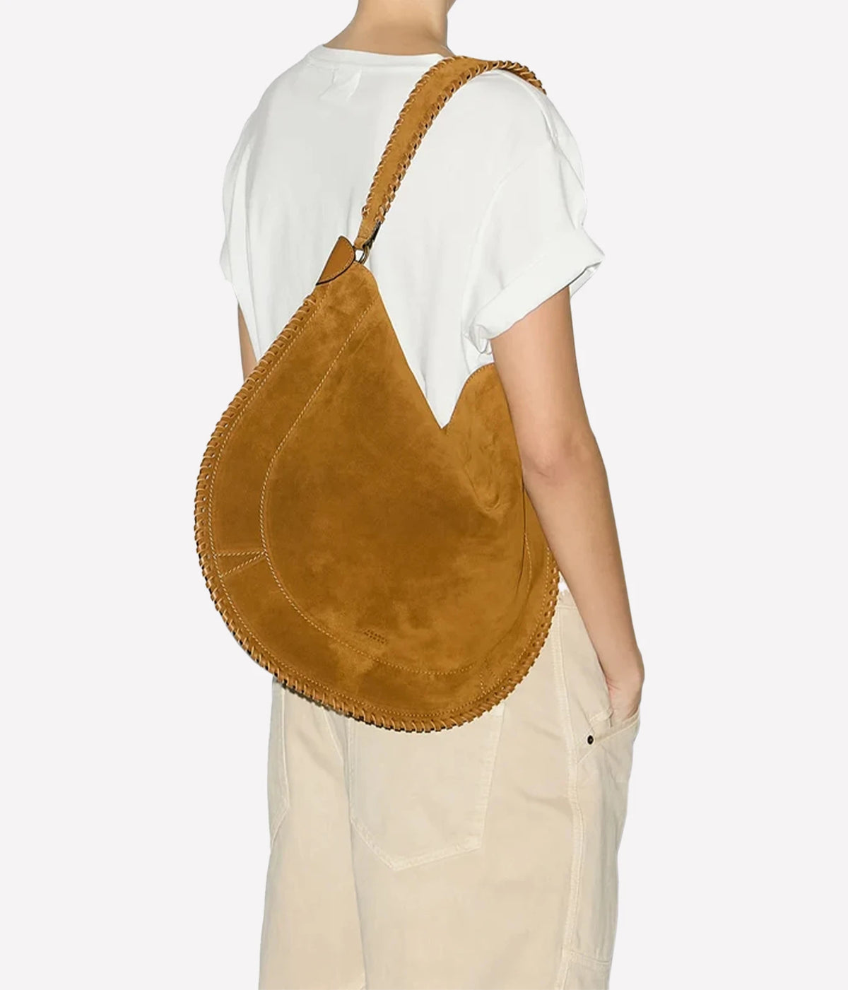 A person wearing a white t-shirt and beige pants, shown from the back and side, carrying a large crescent-shaped tan suede shoulder bag - Oskan Hobo Soft Bag In Cognac