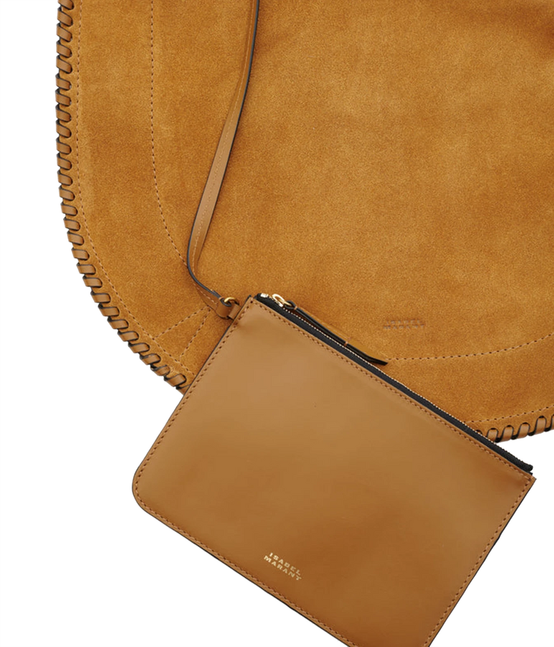 A close-up studio shot of a tan leather pouch with a black zipper and gold logo, attached to a large tan suede shoulder bag with whipstitching - Oskan Hobo Soft Bag In Cognac