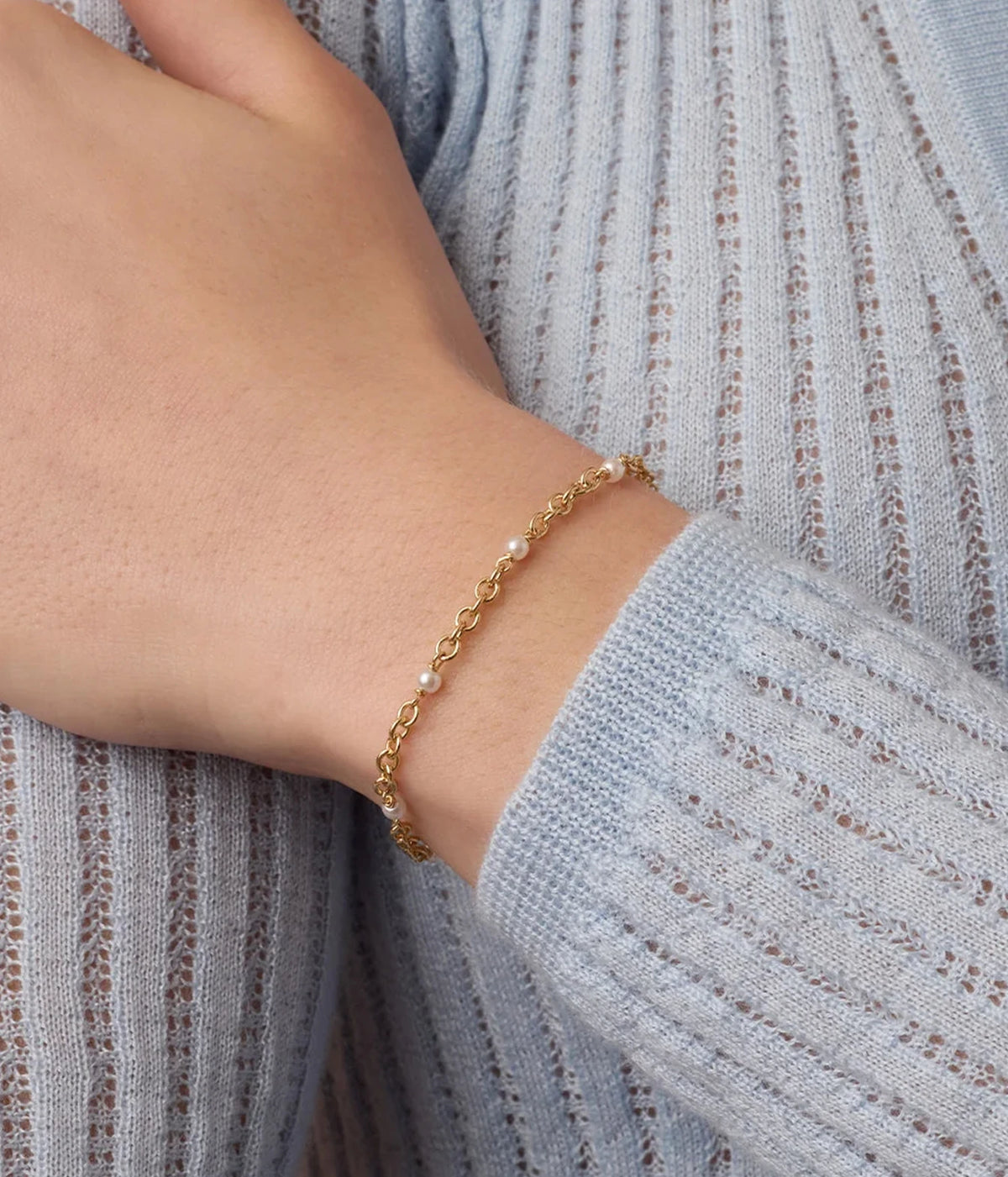 Close-up of a model's wrist wearing the Gorjana Finley Pearl Dot Bracelet in Yellow Gold with a grey-blue ribbed knit jumper