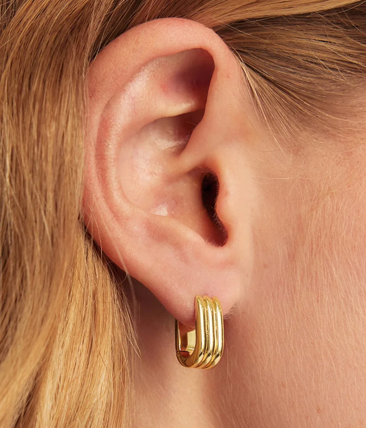 Close-up of a model's ear wearing the Gorjana Melrose Link Huggies in Yellow Gold in the lobe, with her hair tucked behind her ear