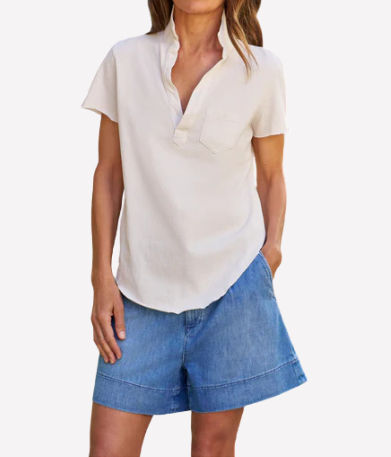 A woman wearing a short-sleeve off-white button-down shirt with a split collar and blue denim shorts, shown from the neck down against a light gray background.