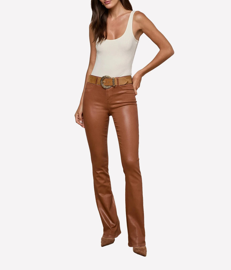 A front view of a model posing in the L'AGENCE Selma Coated Bootcut Jean in Cognac and a white top with a tan belt
