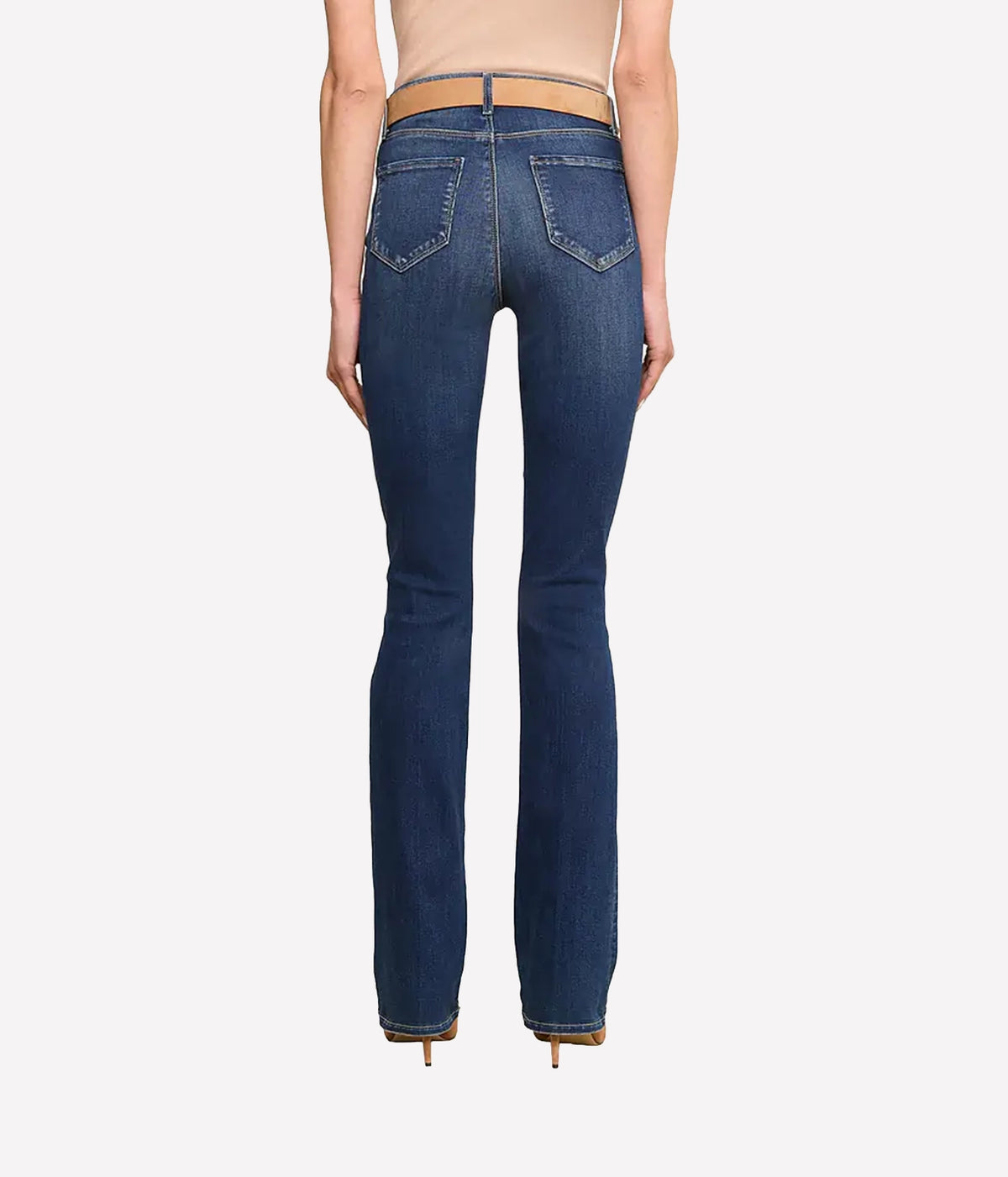 Rear view of a model wearing dark blue jeans with a tan leather waistband, paired with a beige top and gold heels.