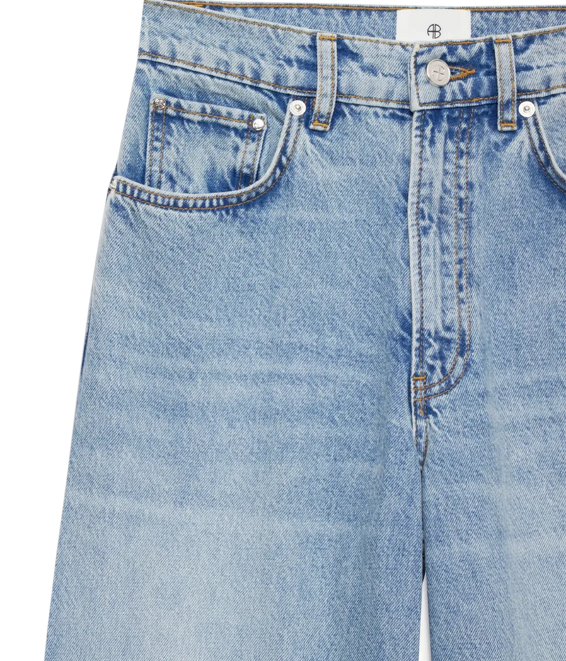 Close-up of a pair of light blue denim jeans showing the front waistband, belt loops, button, pocket, and fabric texture on a white background.