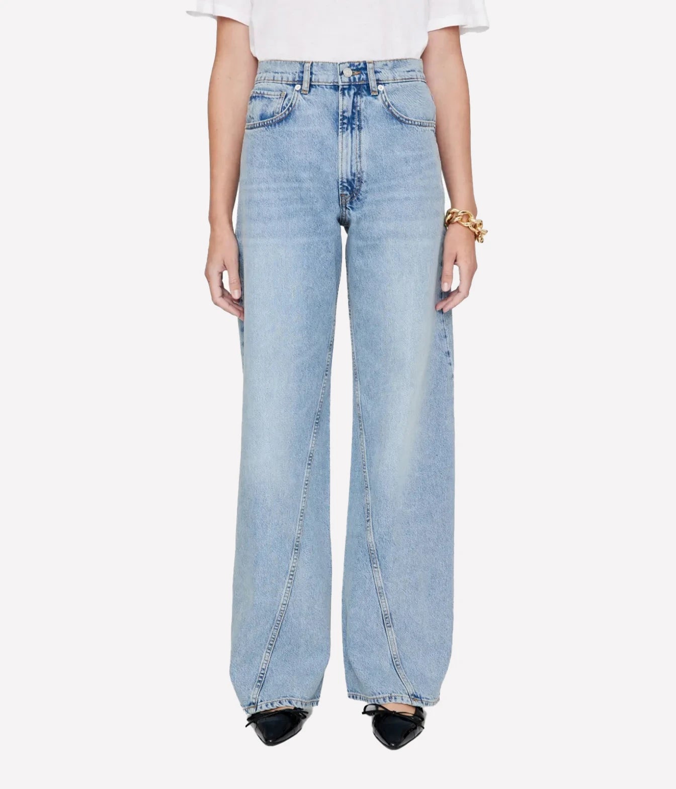 A model from the waist down wearing light-wash, wide-leg denim jeans, a white t-shirt, and black pointed shoes against a plain light gray background.
