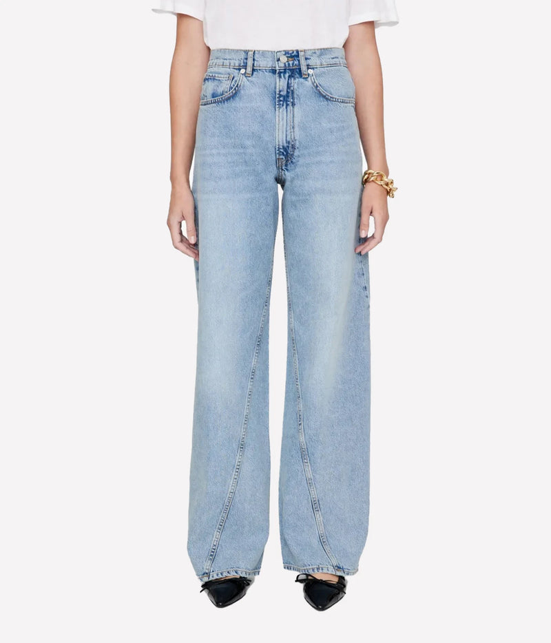 A model from the waist down wearing light-wash, wide-leg denim jeans, a white t-shirt, and black pointed shoes against a plain light gray background.