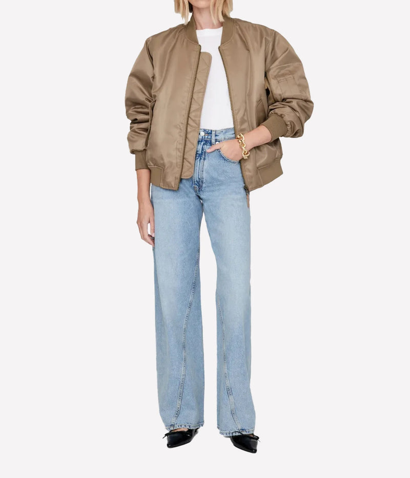 A model wearing a light brown satin bomber jacket, light wash wide-leg denim jeans, a white t-shirt, and black pointed shoes, photographed against a solid light gray background.