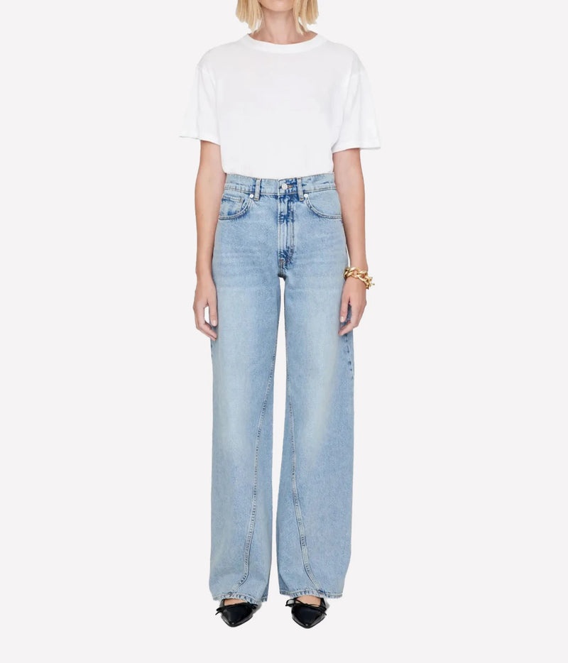 A model wearing a white short-sleeve crop top and light-wash wide-leg denim jeans, paired with black pointed shoes and a gold bracelet, against a plain white background.