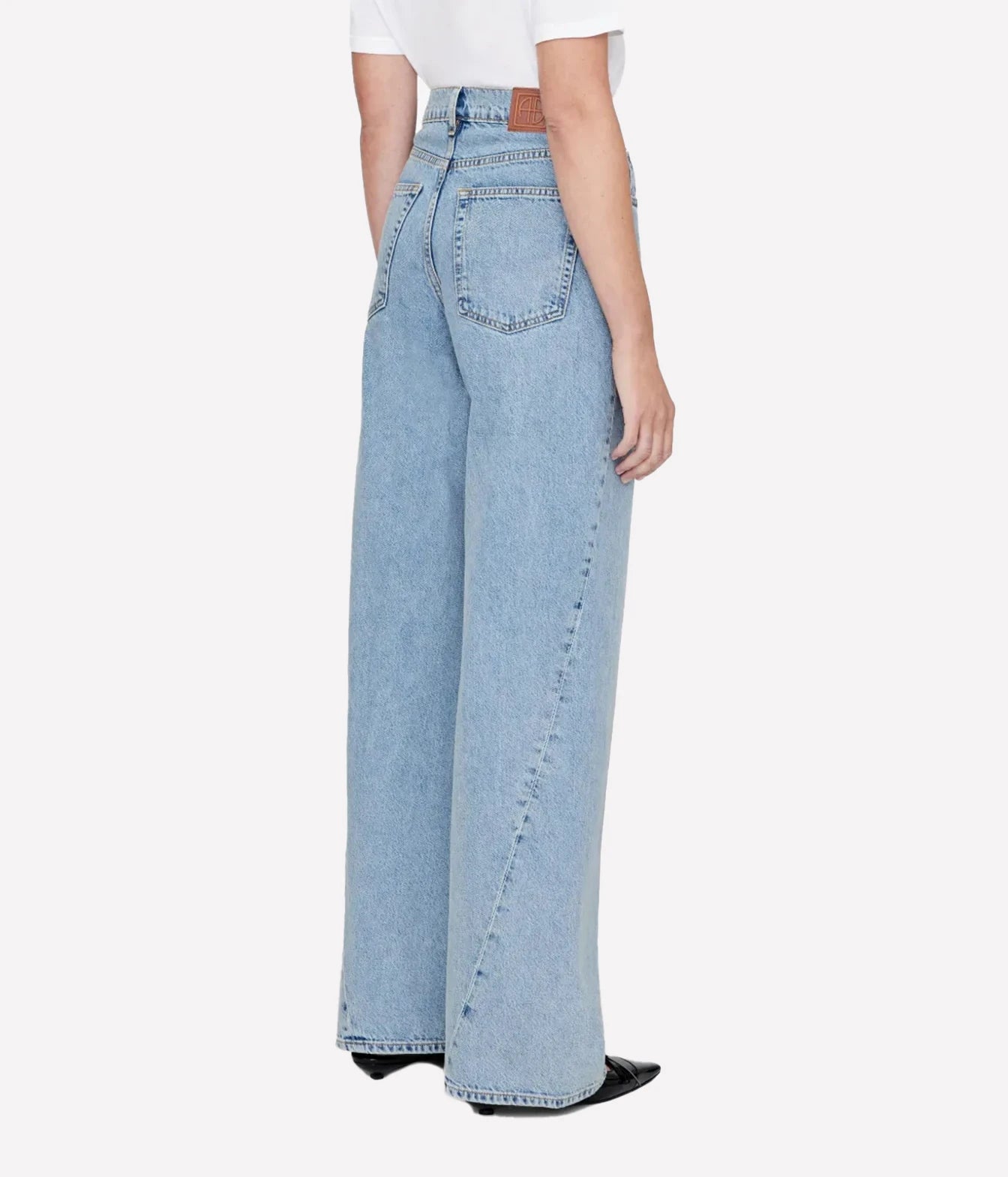 A model shown from the back wearing light-wash wide-leg denim jeans, a white t-shirt, and black pointed shoes against a light gray studio background.