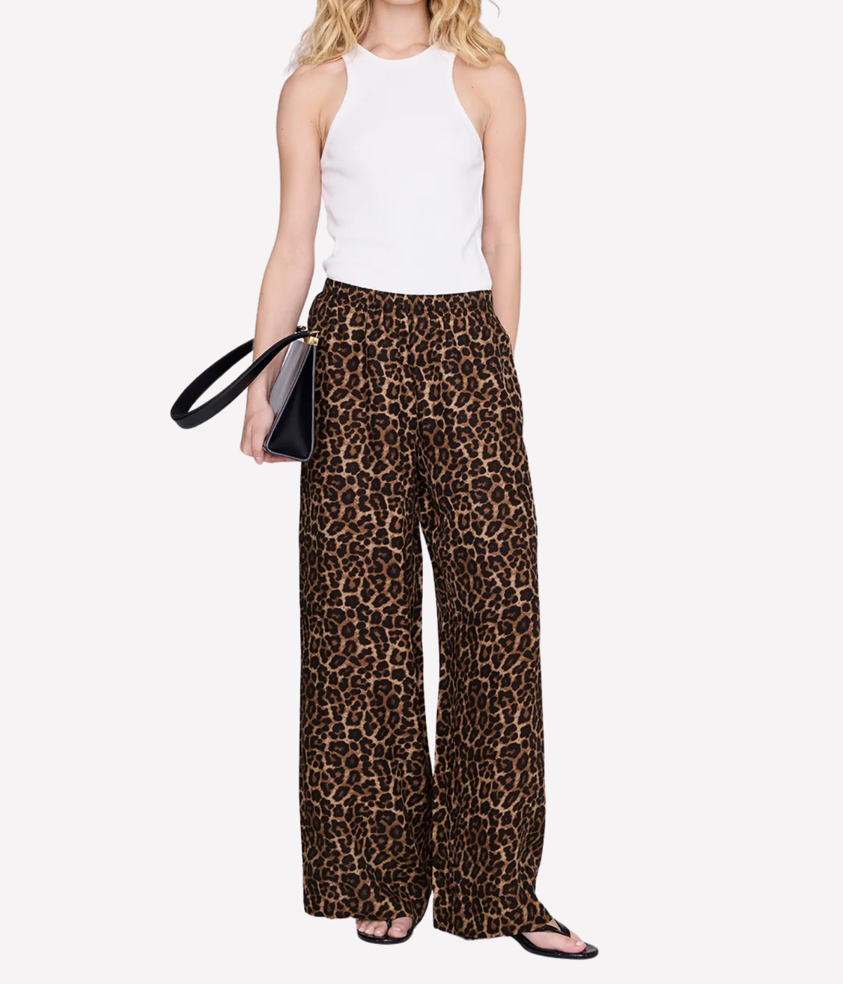 A model wearing leopard-print wide-leg pants with a white sleeveless top, holding a black handbag against a light gray background.