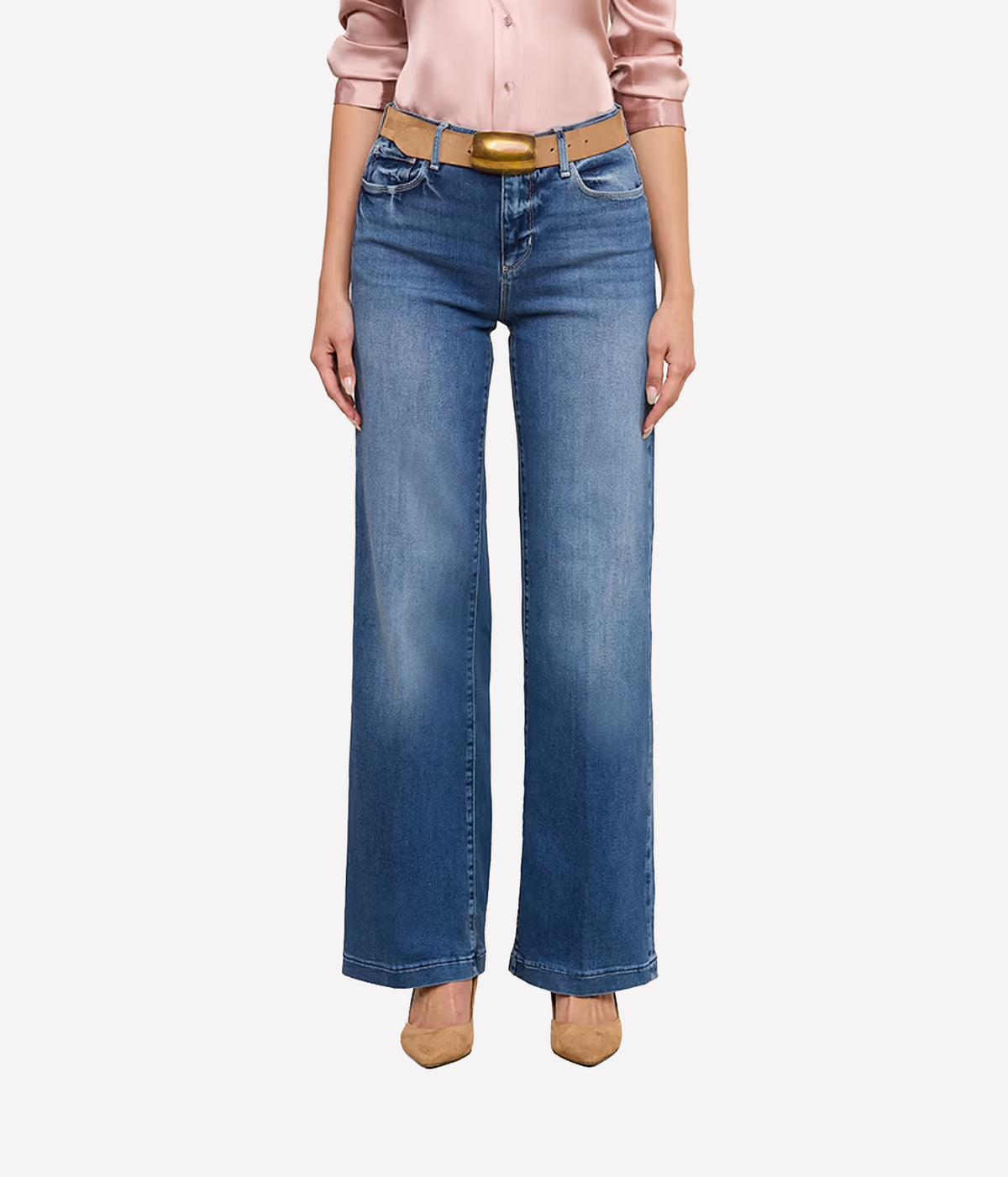 A model wearing a pair of the L'AGENCE Scottie Wide-Leg Denim Jean in Cambridge with a tan leather belt and a gold buckle, paired with a pink satin blouse and beige heels.