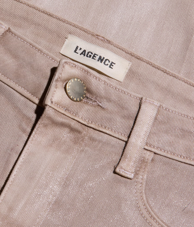 Close-up of a pair of light beige denim jeans showing the waistband, belt loop, button, and a cream-coloured fabric brand label that reads 'L'AGENCE'.