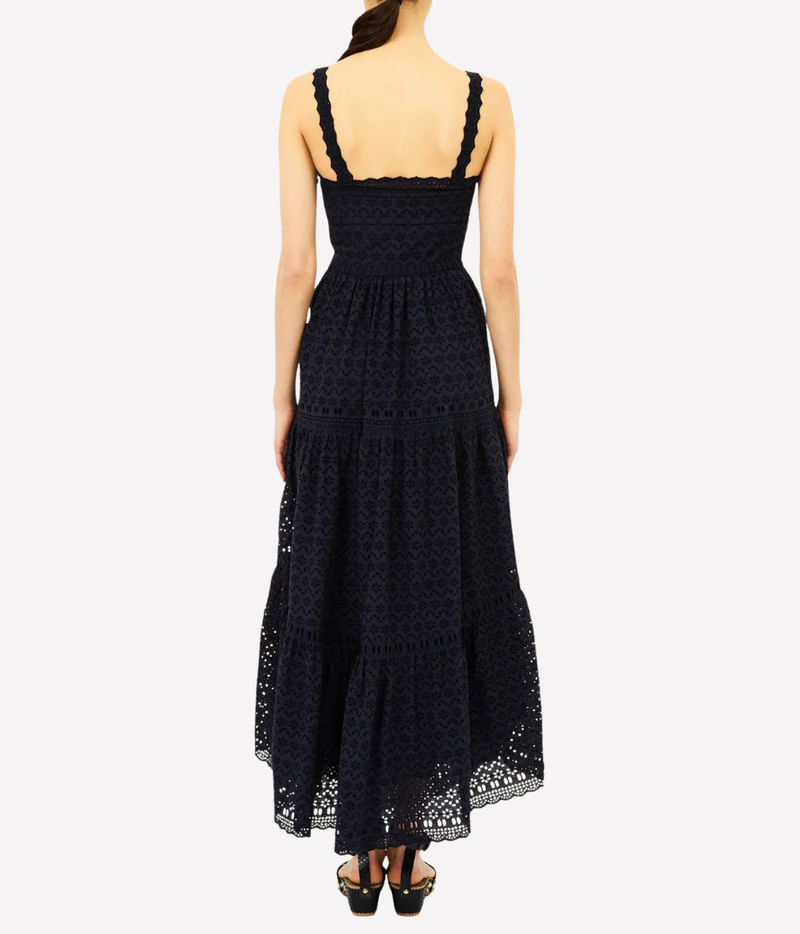 A woman modeling a sleeveless black lace maxi dress from the back, featuring a structured bodice, wide shoulder straps, and a tiered skirt, set against a plain light gray background.