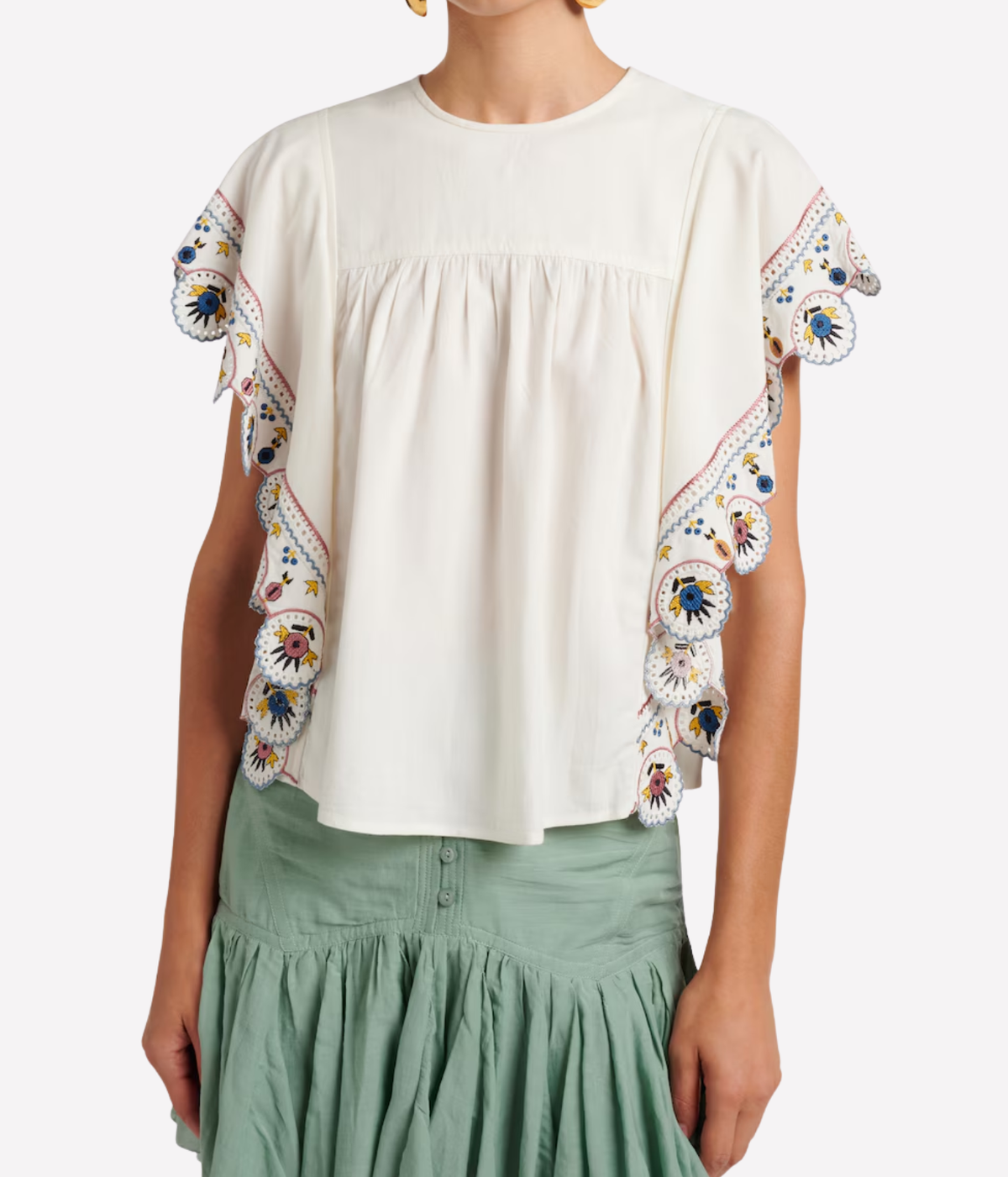 A woman wearing a cream-coloured short-sleeve blouse with colourful embroidered ruffle details on the sleeves - Marlie Top In Ecru