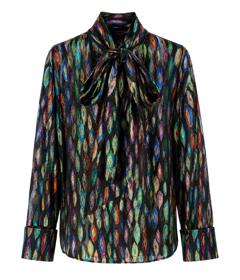 A long-sleeve blouse with a high collar and a large front bow, featuring an iridescent multicolor ikat pattern on a black base, shown against a plain white background.