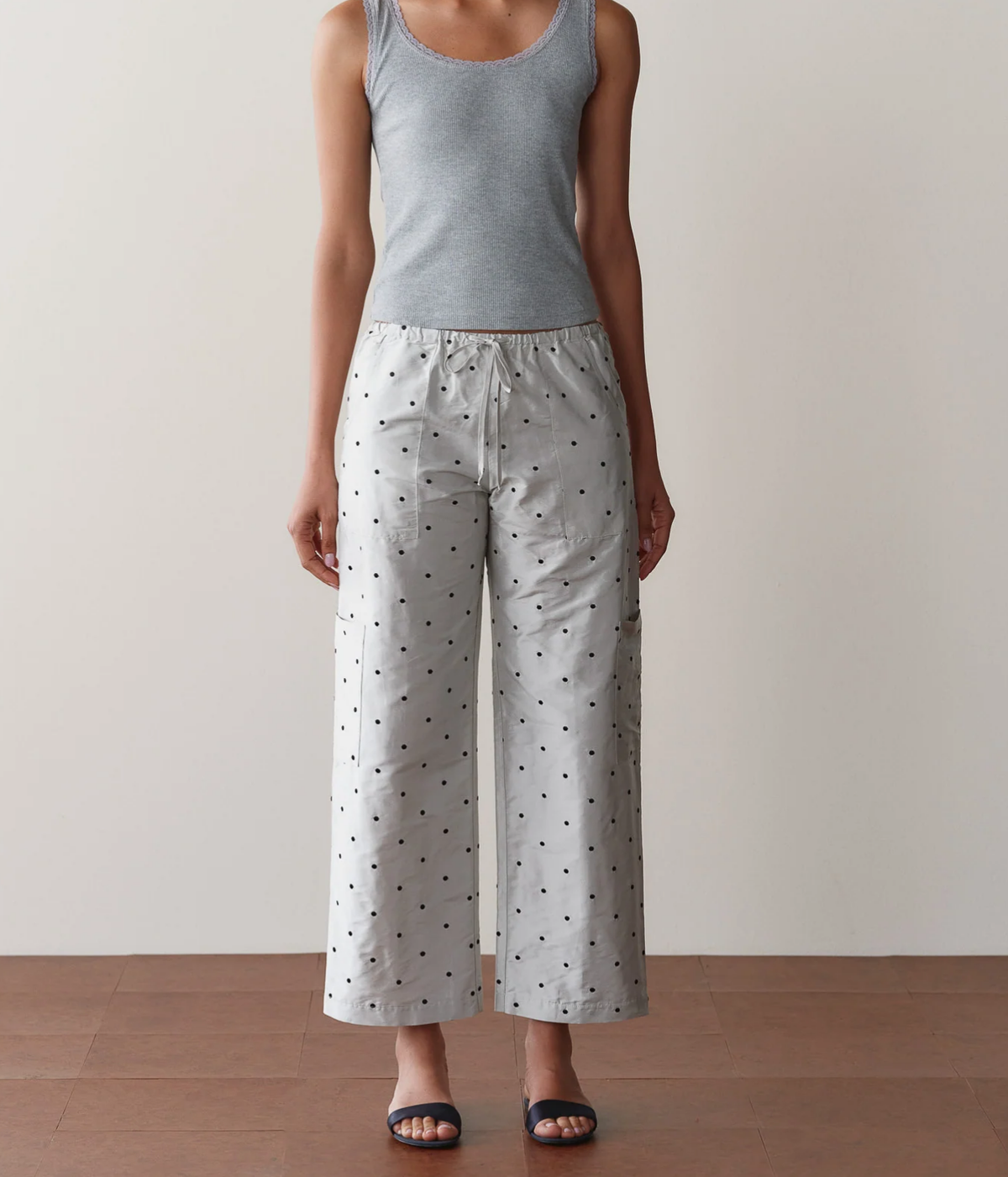 Front view of a model wearing the DONNI. The Silk Taffeta Cargo Pant in Silver Polka Dot with a fitted grey tank top and black slide sandals, showing the relaxed wide cropped leg