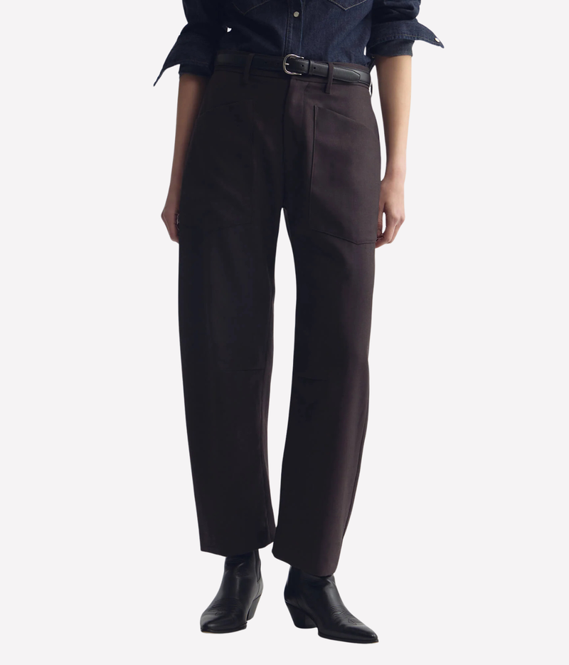 A model wearing dark brown wide-leg trousers with a black belt, paired with a dark denim shirt and black ankle boots, shown from the waist down on a light gray background.