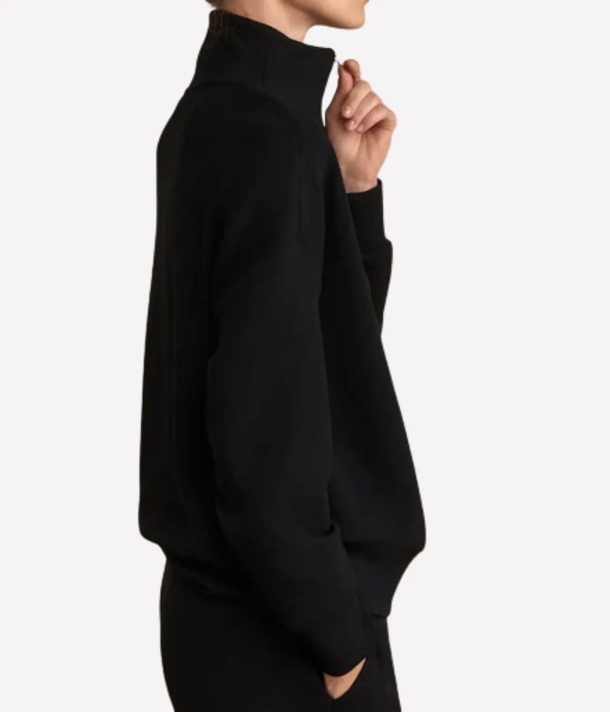 Side profile of a model wearing the Varley Hawley Half Zip Sweater In Black with a hand at the zip and the other in the pocket, showing the funnel neckline and oversized fit