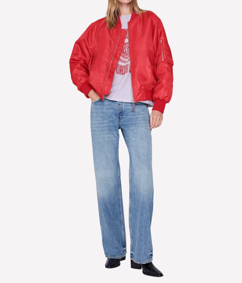 A model wearing a red nylon bomber jacket, light-wash blue jeans, and black shoes, standing against a light gray background.