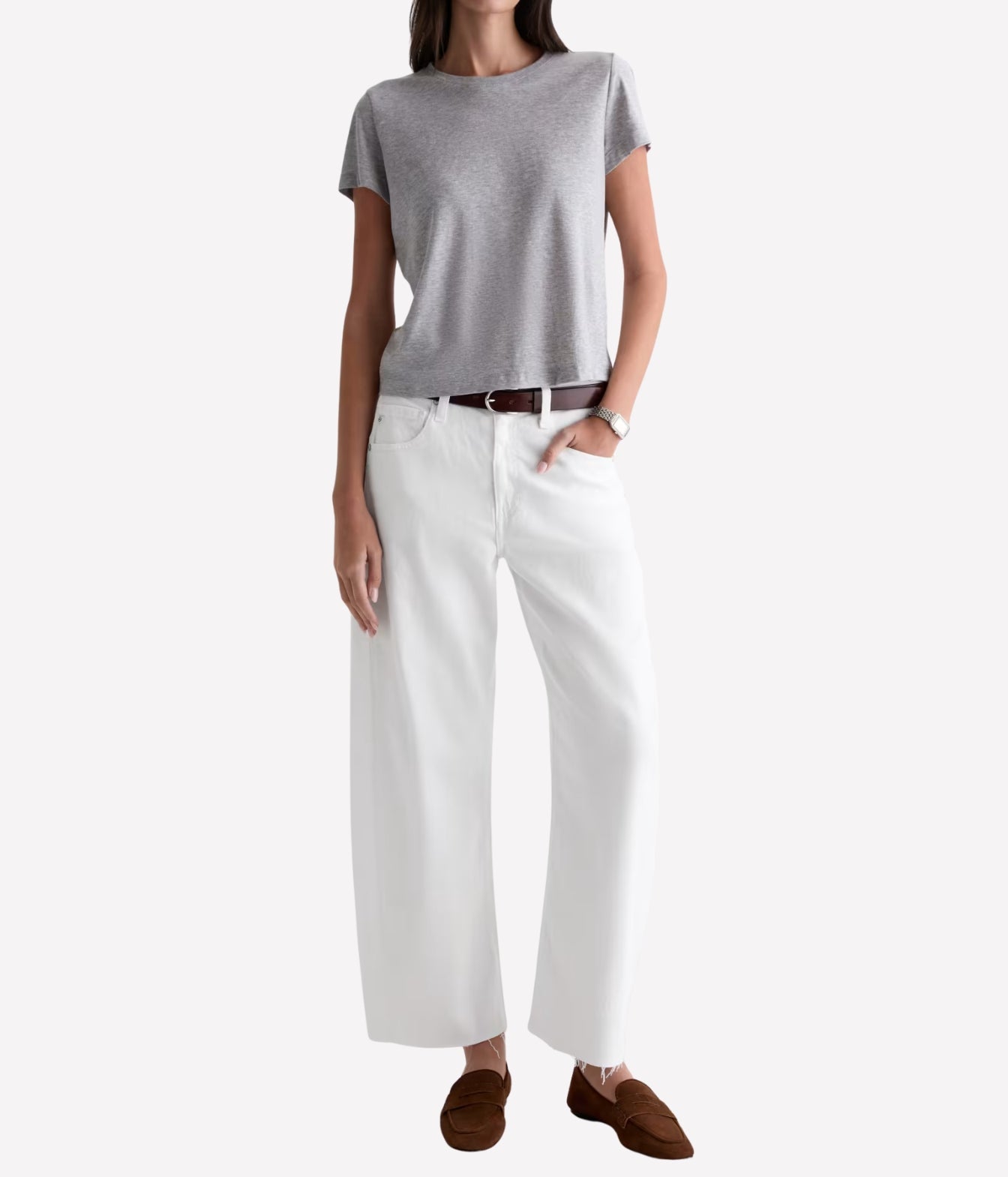 A model wearing a light gray short-sleeve knit top, white wide-leg cropped pants, a brown belt, and brown slip-on shoes, shown against a plain light gray studio background.