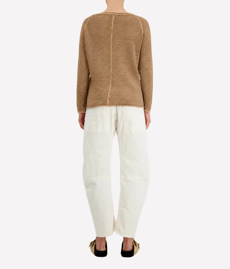 Back view of a model wearing the Avant Toi Maglia Pullover in Sughero with cream barrel-leg trousers and dark sandals, showing the contrast centre-back seam